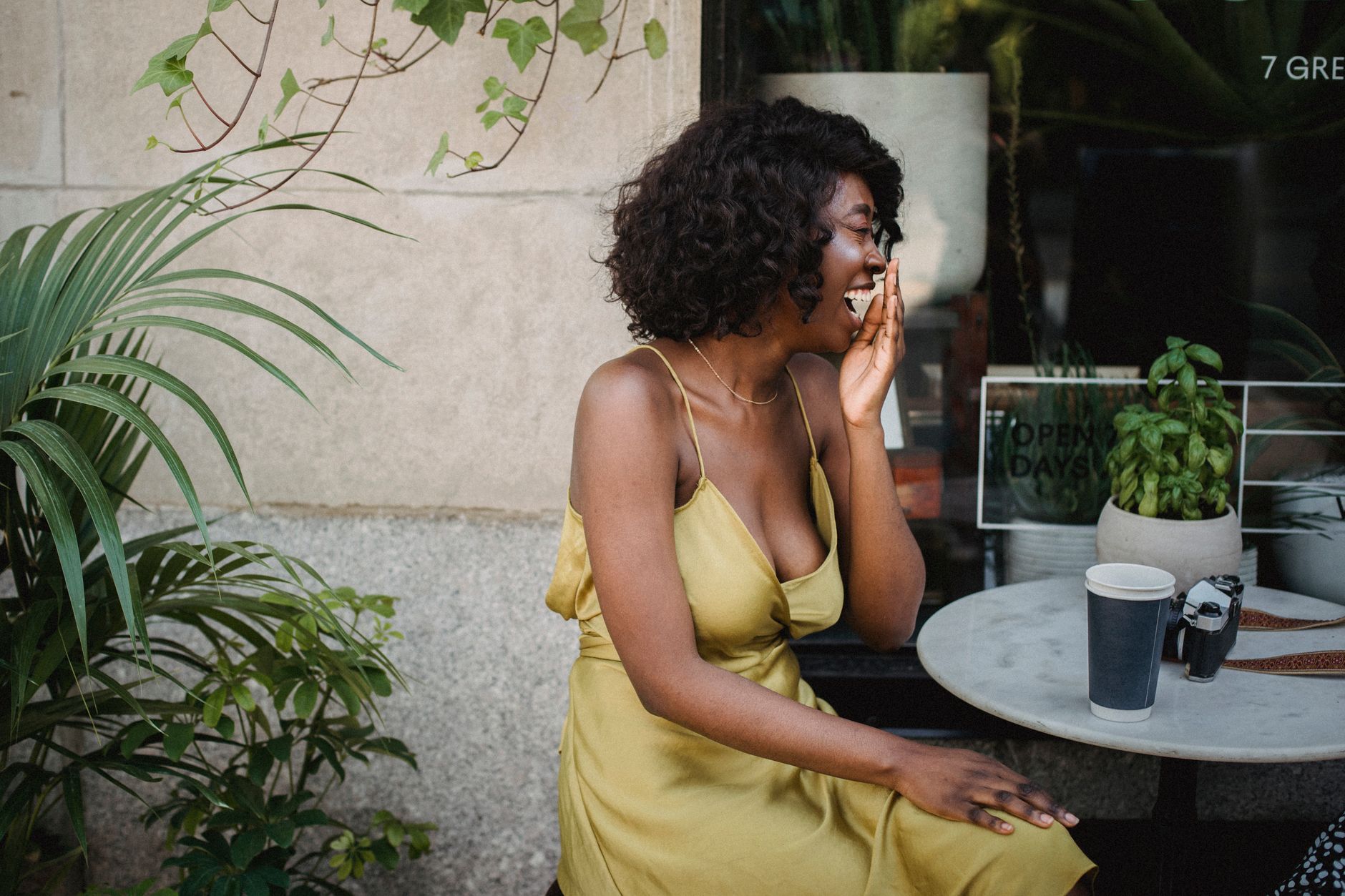 Woman laughing at an outdoor street cafe with tropical plants — the relaxed, social cafe culture of a Latin American colonial district.