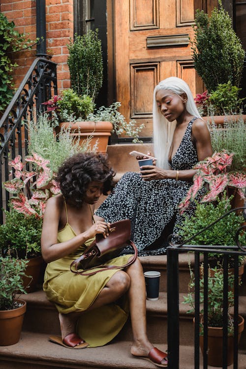 Two women in dresses sitting outside on the stairs besides plants.
