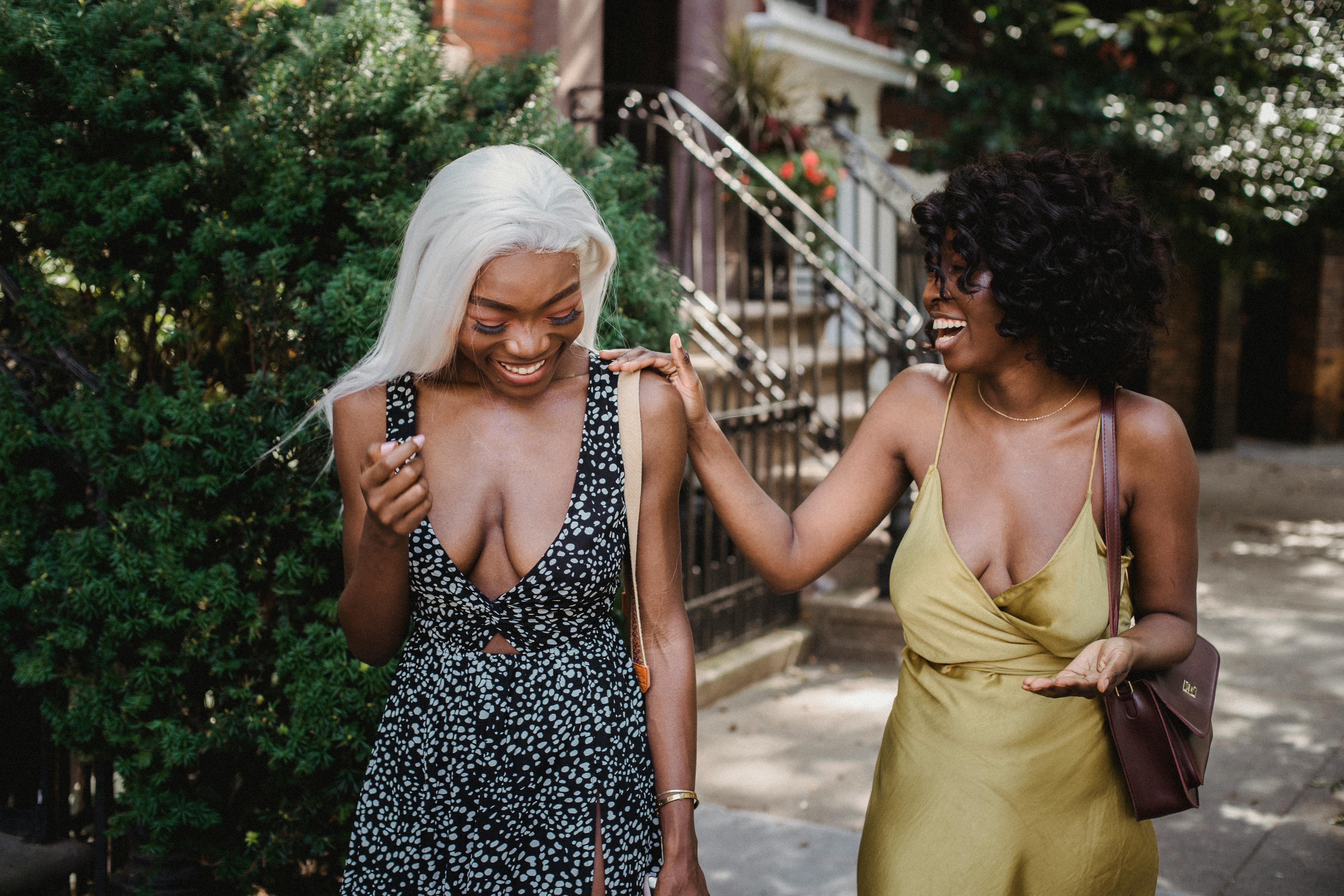 Two cheerful women in summer dresses laughing and walking outdoors on a sunny day.