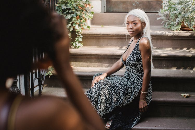 Woman Taking A Picture Of Another Woman Sitting On Steps In Front Of A House Entrance 