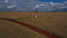 Drone view of small stone church in agricultural land under blue cloudy sky at daylight