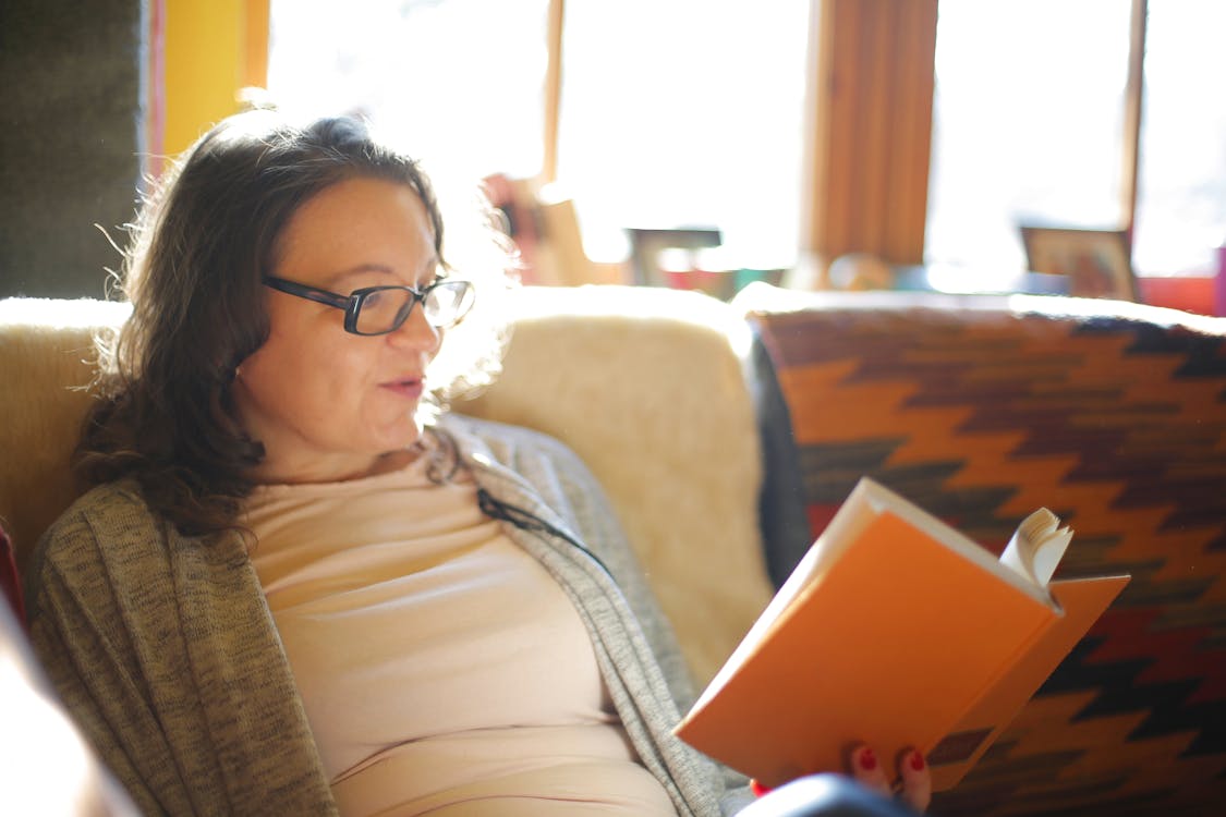 Woman in Glasses Sitting in an Armchair and Reading a Book
