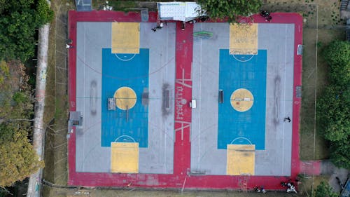 Free Aerial view of basketball court colored with red and blue with yellow lines located near green trees and grass with fence in daylight Stock Photo