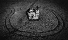 Small damaged church with cross in field