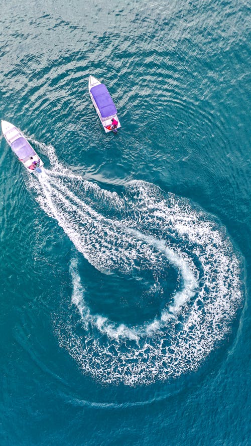 Drone view of modern motorboats floating on rippling turquoise ocean water and leaving trace