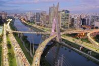 From above of modern bridge crossing river with modern skyscrapers and green trees against cloudy and blue sky