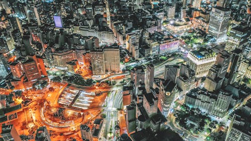 Aerial view of illuminated streets of modern multistory buildings located along roads in center at night