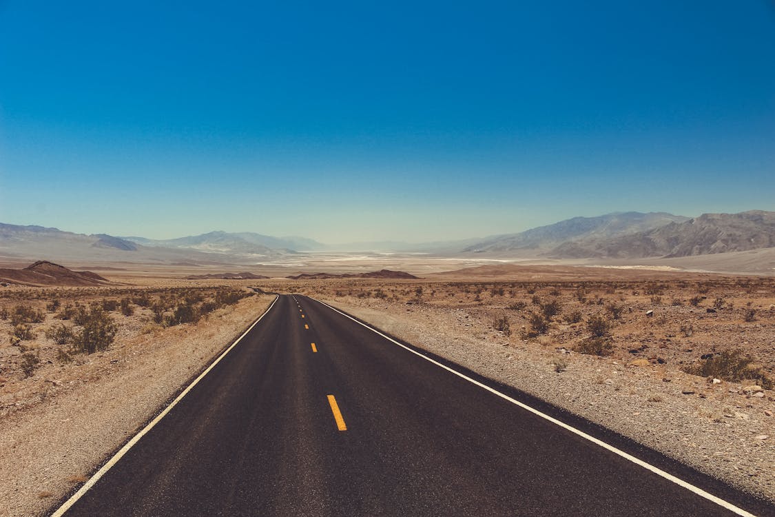 Black Asphalt Road in the Middle of Desert Land Under Blue Sky