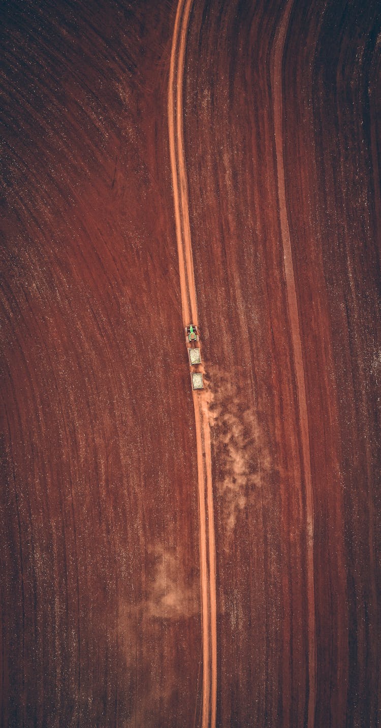 Tractor Trailer Driving On Dirt Road Through Fields