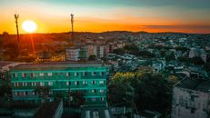 Aerial view of dormitory area scenery with greenery among low shabby residential buildings and huge orange sun on skyline