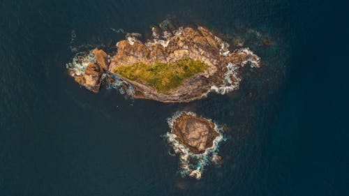 Top view of rough stony coastline of islands with vegetation in middle washed with dark water of sea