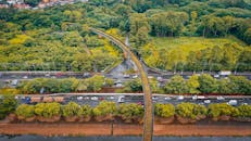 Drone view of busy multilane road with driving cars between lush leafy trees in suburban area