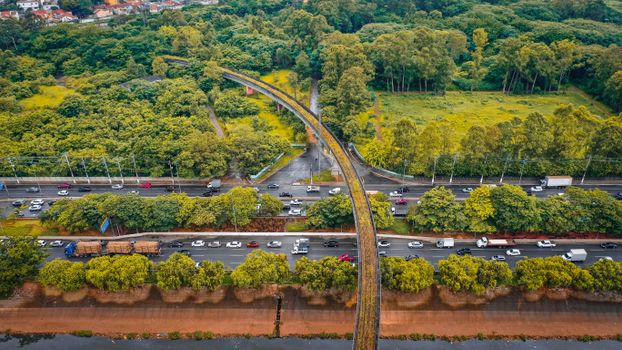 Drone view of busy multilane road with driving cars between lush leafy trees in suburban area