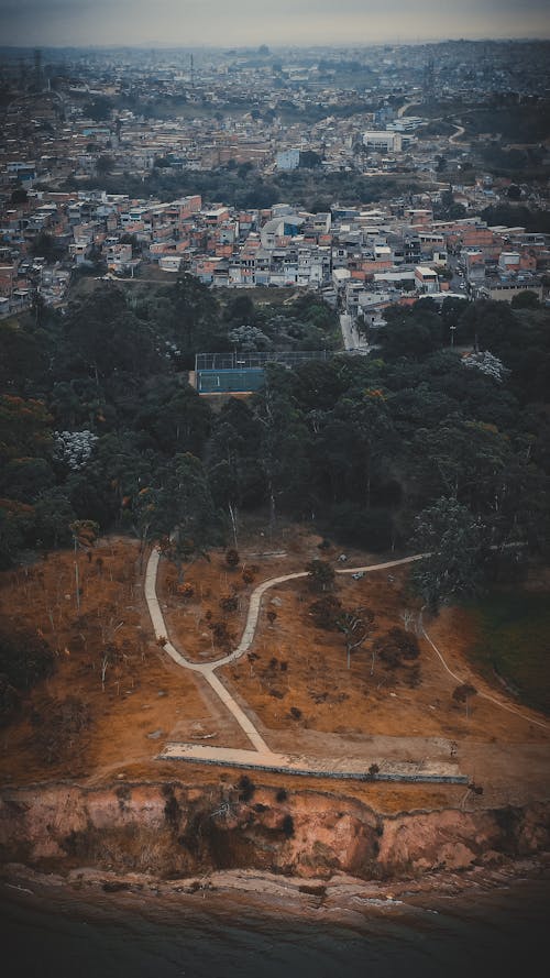 Drone view of road located on shore of sea surrounded by trees and residential houses in settlement