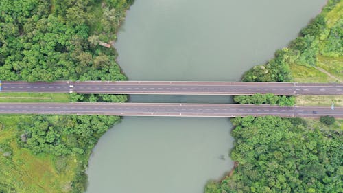 Free Drone view of straight road bridge crossing river between coasts covered with lush woods Stock Photo
