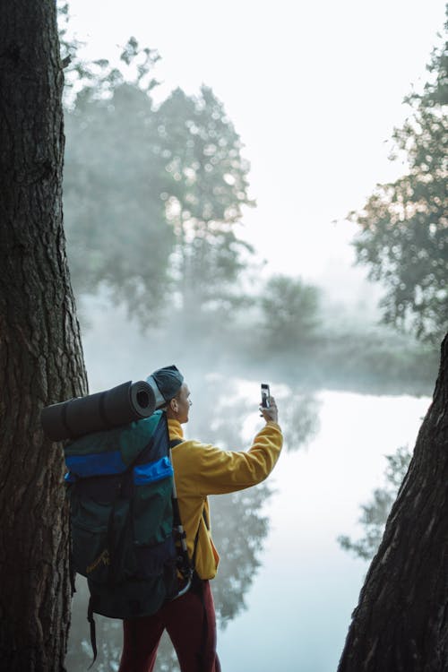 Free A Man Taking Pictures of a Foggy River Using a Smartphone Stock Photo