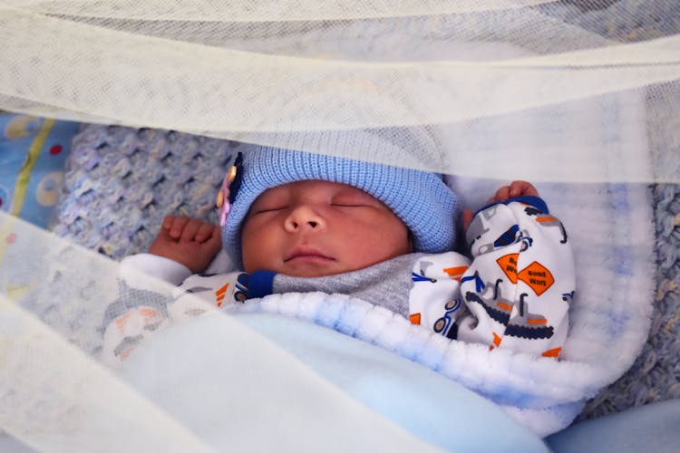 A Newborn Baby Sleeping While Wearing A Blue Bonnet