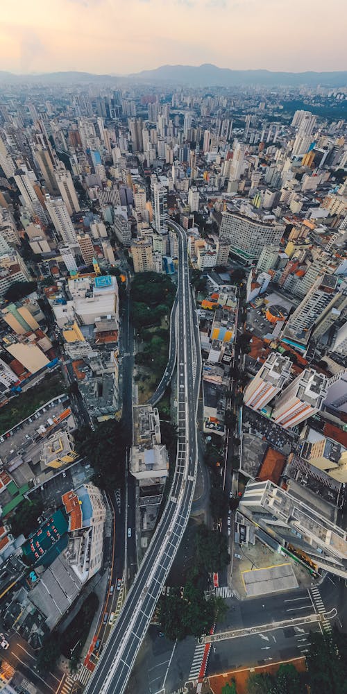 Free Drone view of narrow long roadway between modern tall skyscrapers and densely built residential houses located on streets of city Stock Photo