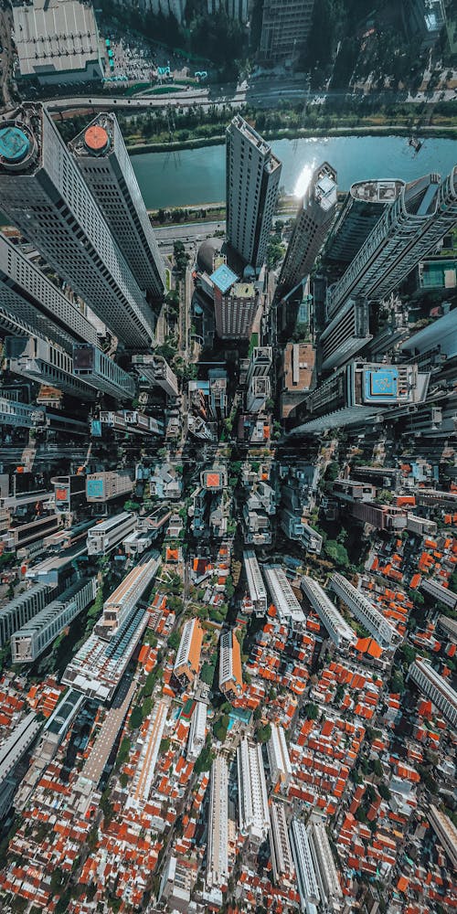 Free Drone view of densely built contemporary multistory skyscrapers with creative design located on streets of modern city with water canal Stock Photo