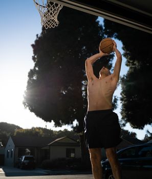 Shirtless man catching a basketball shot in an outdoor setting with the sun in the background.