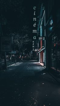 Atmospheric night shot of a quiet street with illuminated cinema signage and sidewalk.