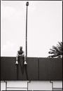 Black and white full length African American male with naked torso sitting on tall stone fence and looking at camera