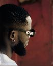 Side view crop unemotional African American male wearing trendy sunglasses and earring standing against weathered red wall