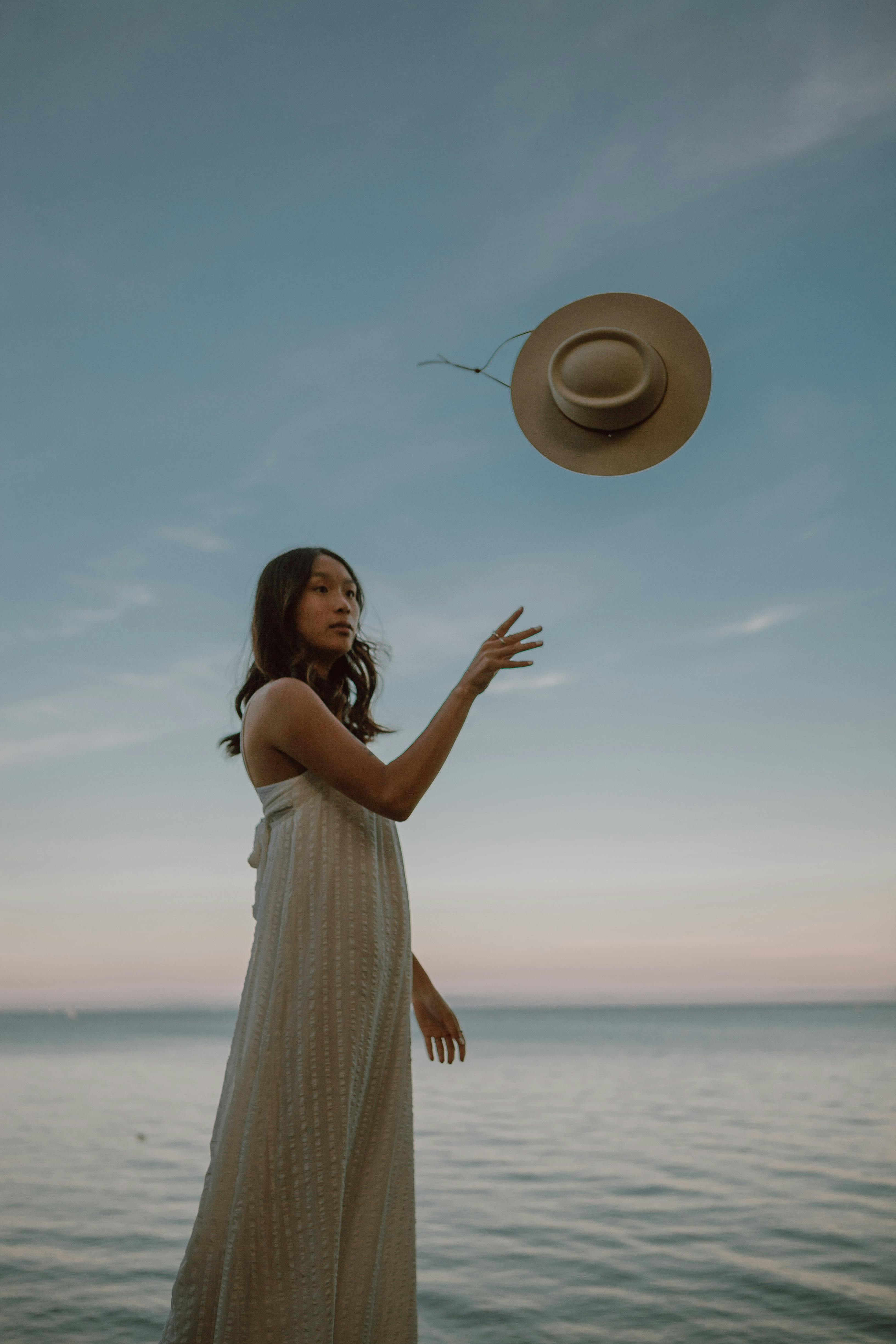 calm ethnic female throwing hat while standing in sea