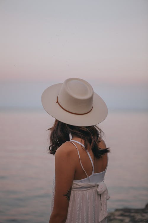 Woman in stylish hat enjoying sunset on beach