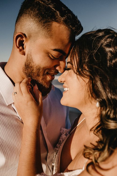 Free Side view of crop delighted young ethnic lady and guy cuddling and touching foreheads against blue sky Stock Photo