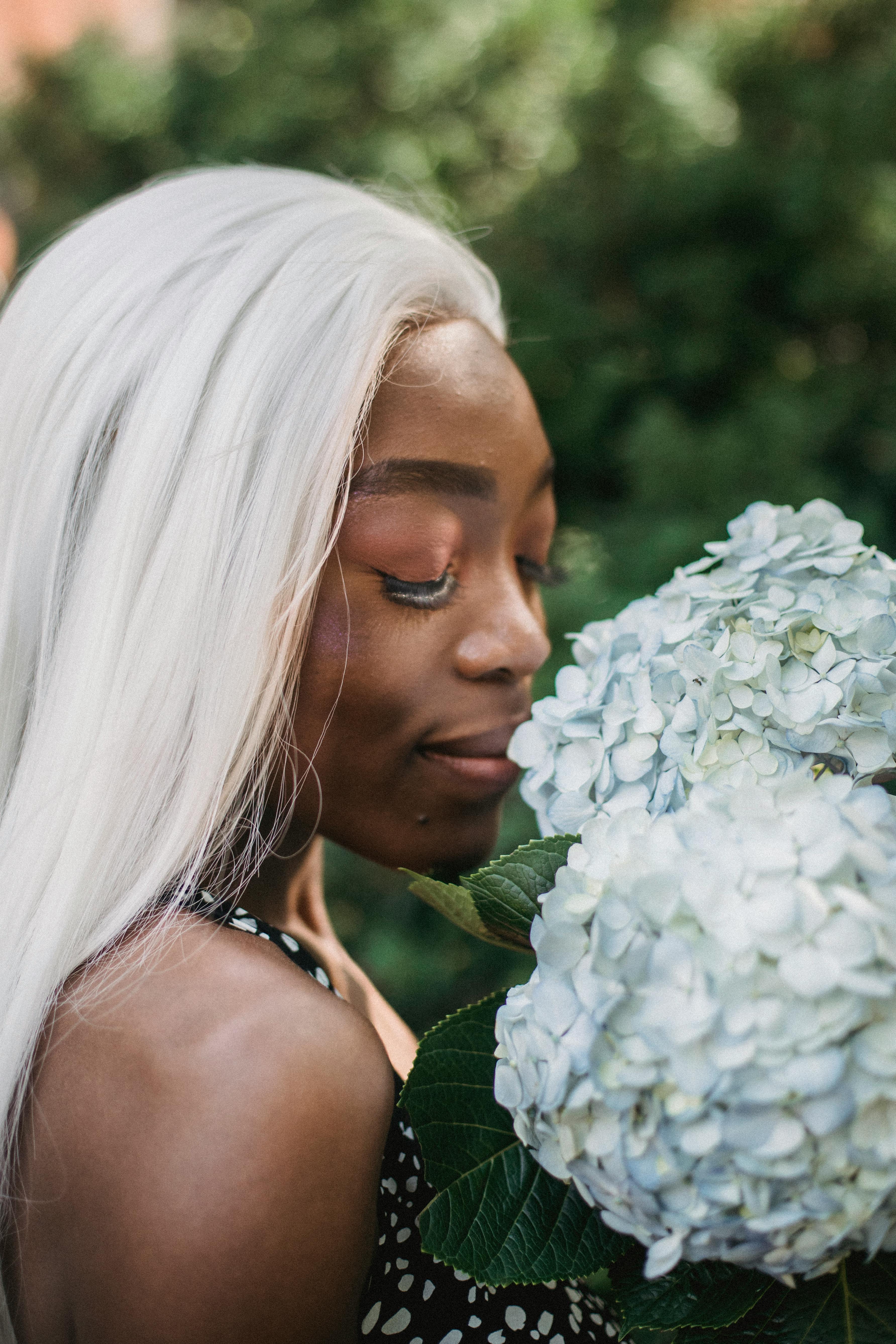 Close-up of a black woman with dyed hair smelling hydrangea flowers outdoors.