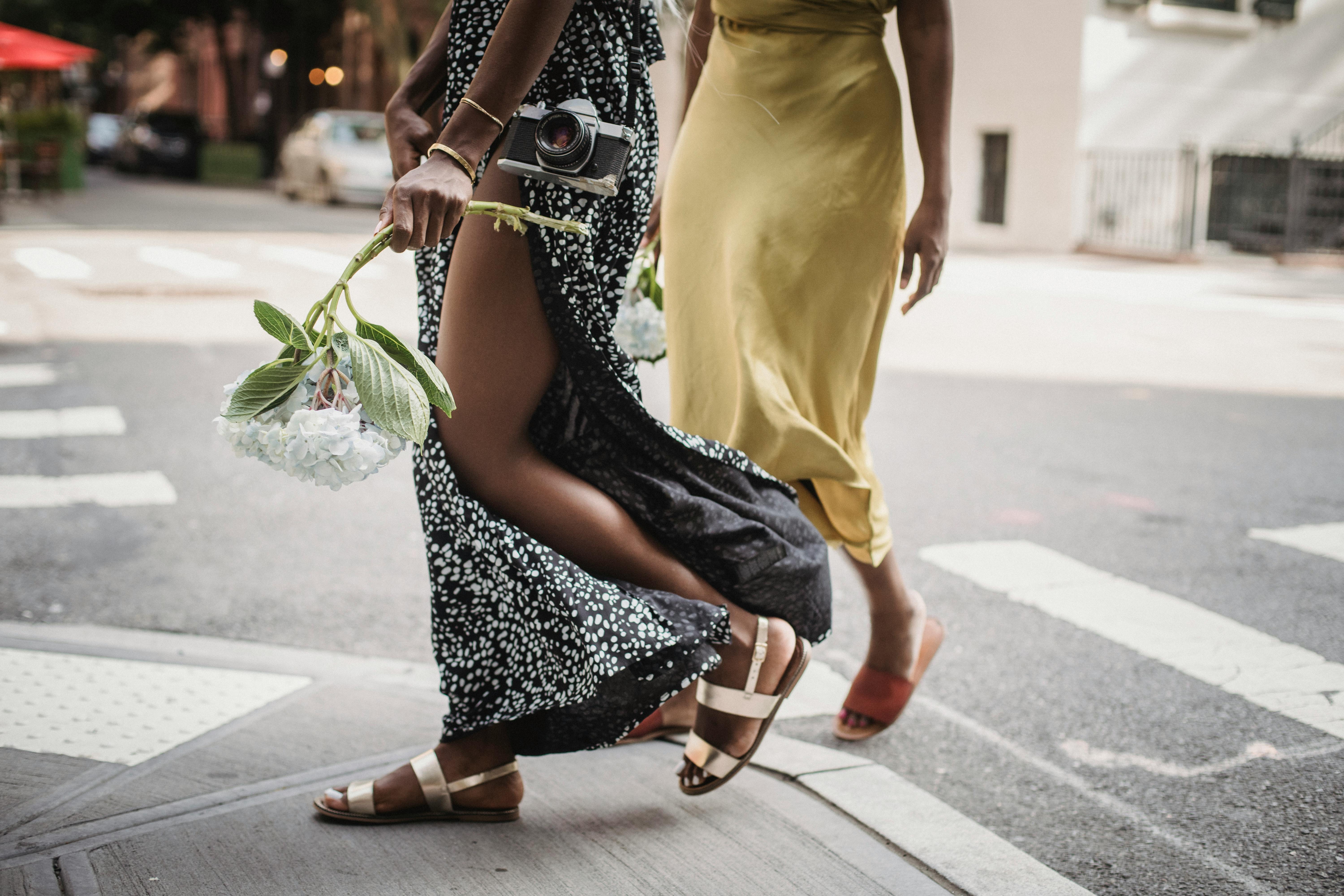 Free Two women in elegant dresses walk stylishly across an urban street. Stock Photo