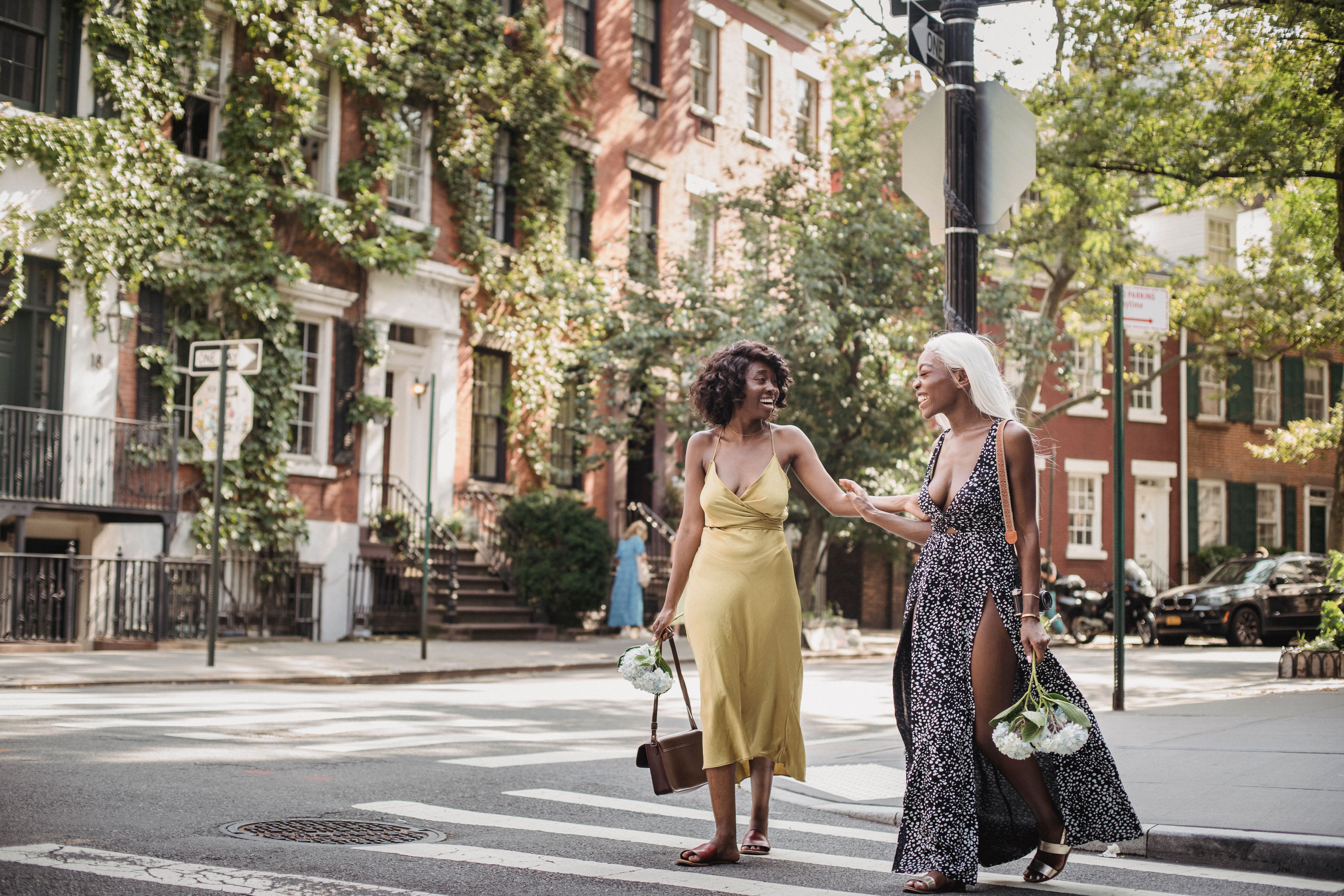 Two women walking and laughing on a city street during the day, holding flowers.