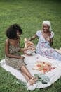 2 Women Sitting on White Textile on Green Grass Field