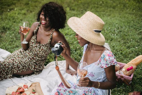 Woman in Dress Holding Wine Glass While Her Friend is Holding a Camera 