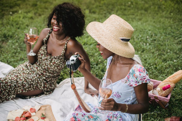 Woman In Dress Holding Wine Glass While Her Friend Is Holding A Camera 