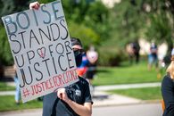 Anonymous male activist wearing protective mask and sunglasses demonstrating placard with antiracist slogan during protest meeting in city park