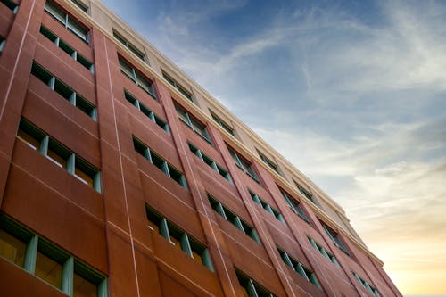 Low angle exterior of brown contemporary multistory condominium without balconies located under clear blue sky