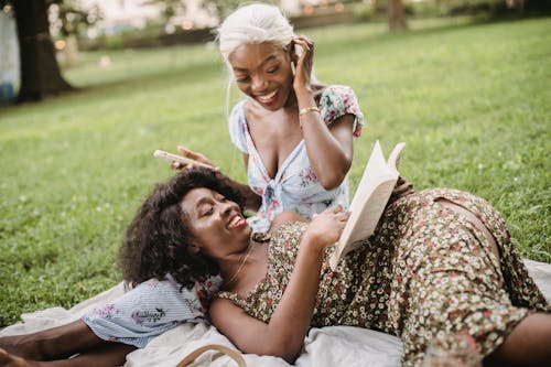 Free Woman Reading a Book While Lying on the Lap of her Friend Stock Photo