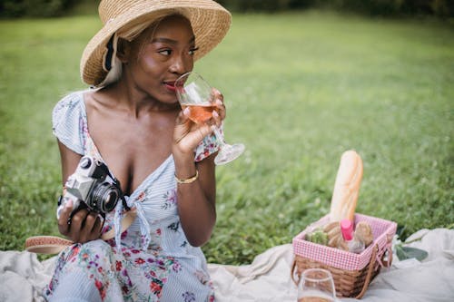 Woman in White and Red Floral Dress Holding Glass of Wine and Camera 