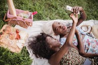 两名女子在户外野餐，自拍并品尝葡萄酒和奶酪，享受轻松时光