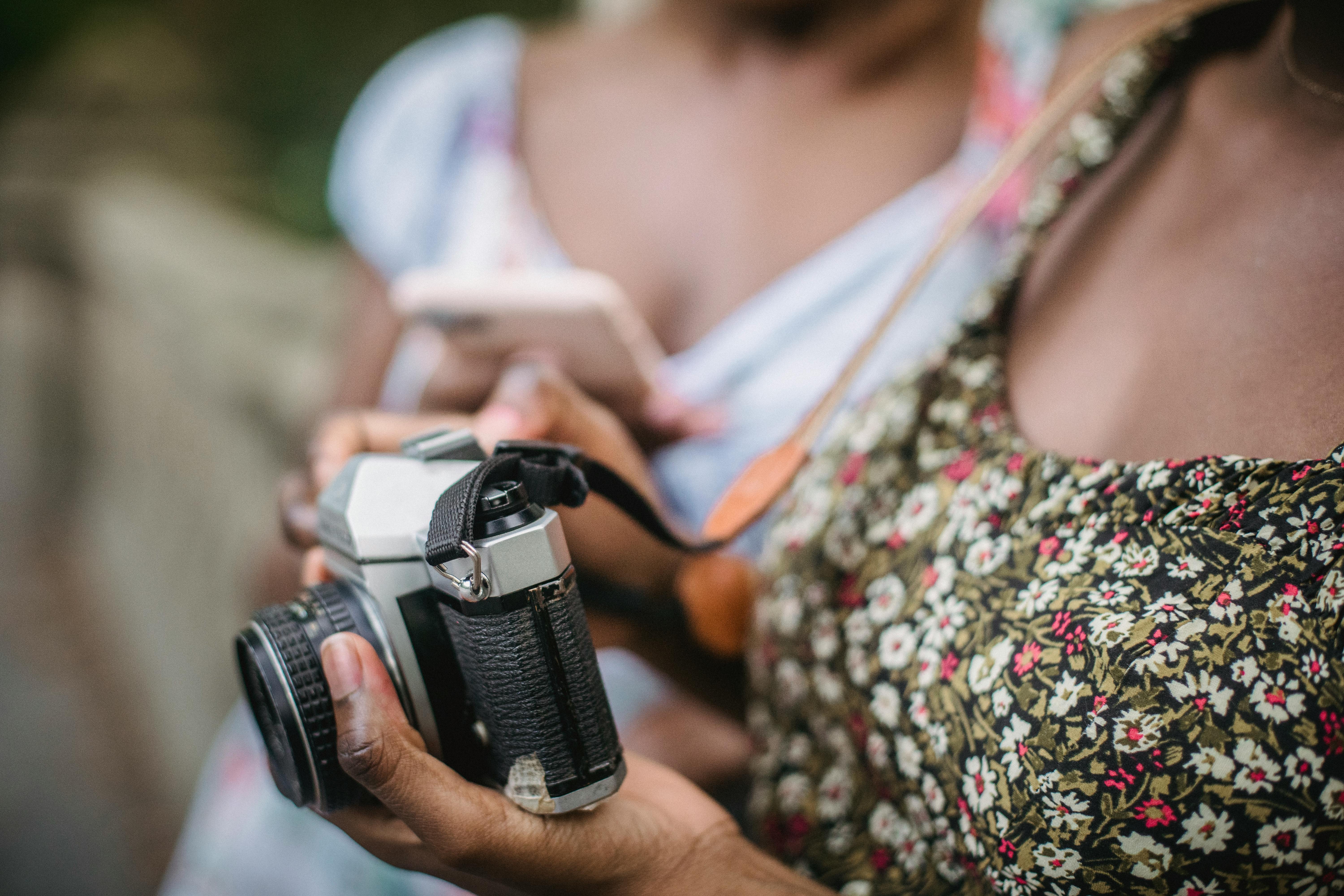 身穿花卉上衣的人手持复古相机，特写镜头营造出经典的氛围