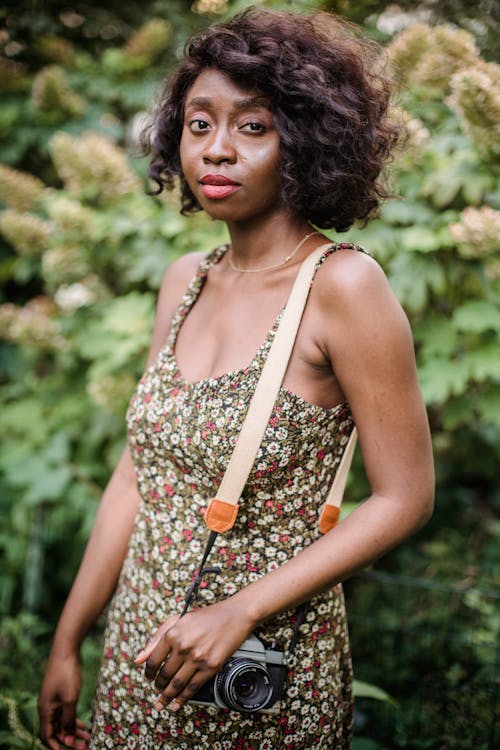 A Woman Wearing a Floral Dress Carrying a Vintage Camera