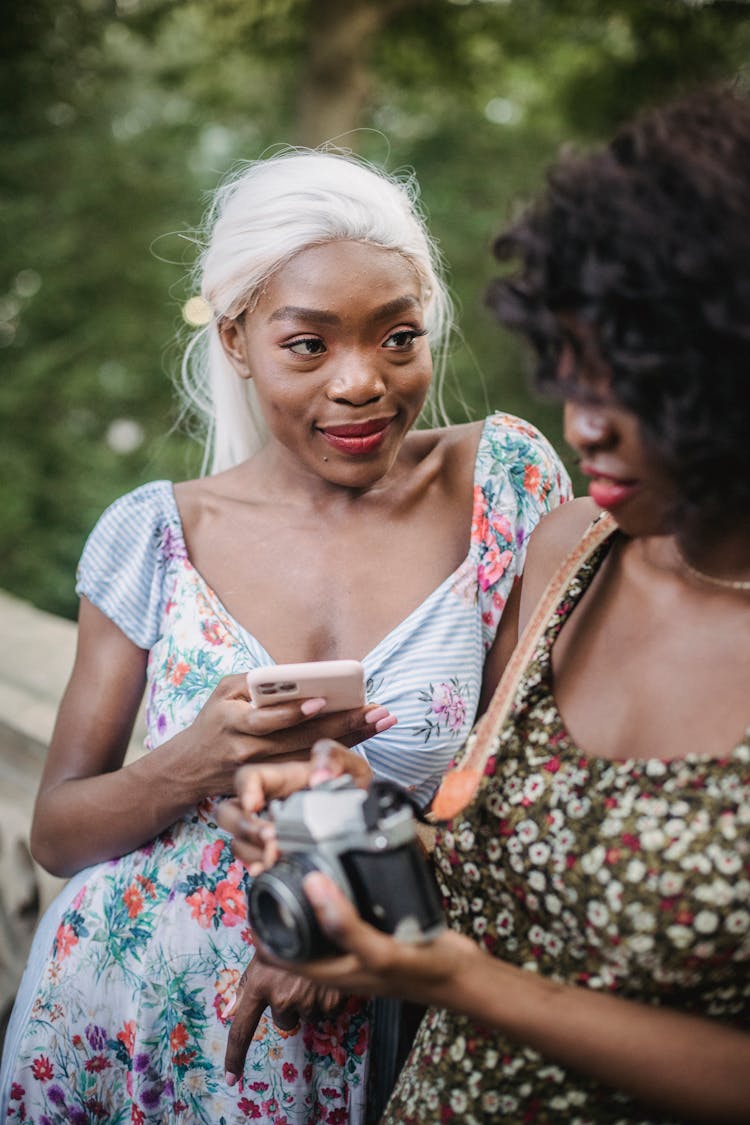 Women Using Smartphone And Holding A Camera