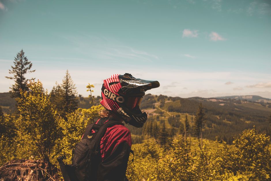 Mountain biker in helmet enjoying a scenic view of lush forest under a clear blue sky.