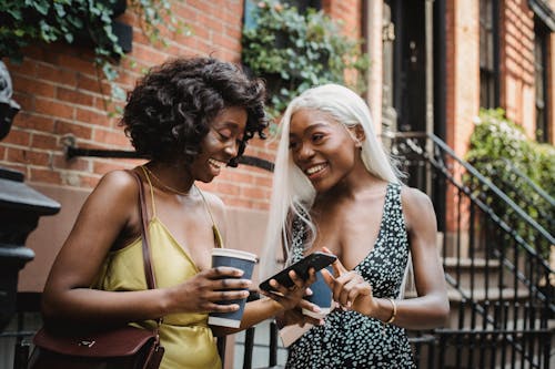 Woman in Yellow Tank Top Holding Smartphone While Her Friend is Looking at Her