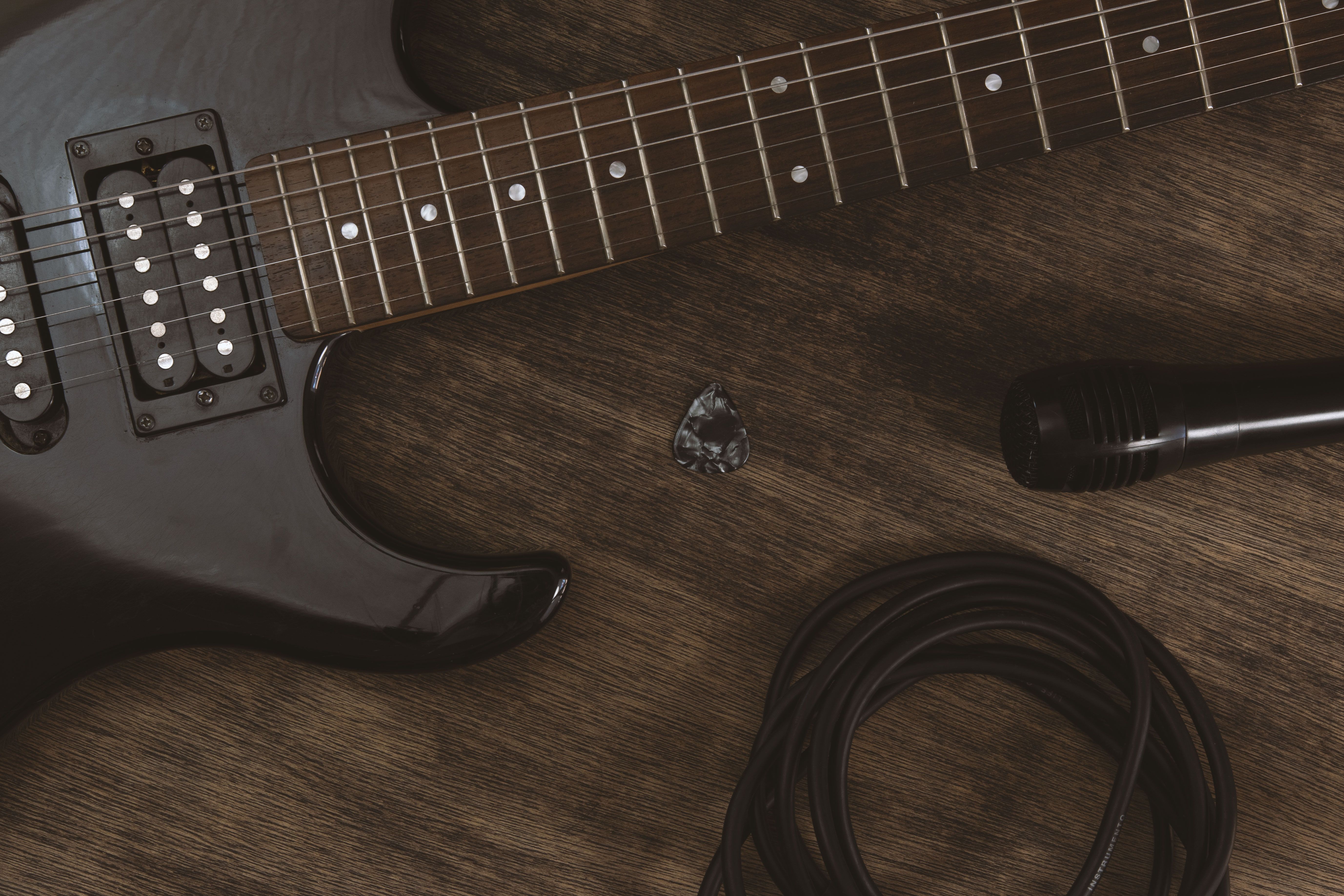 Close-up of an electric guitar with a microphone and plectrum on a wooden surface.