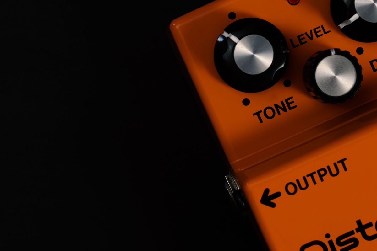 Close-up of an orange guitar distortion pedal showing its tone and level control knobs