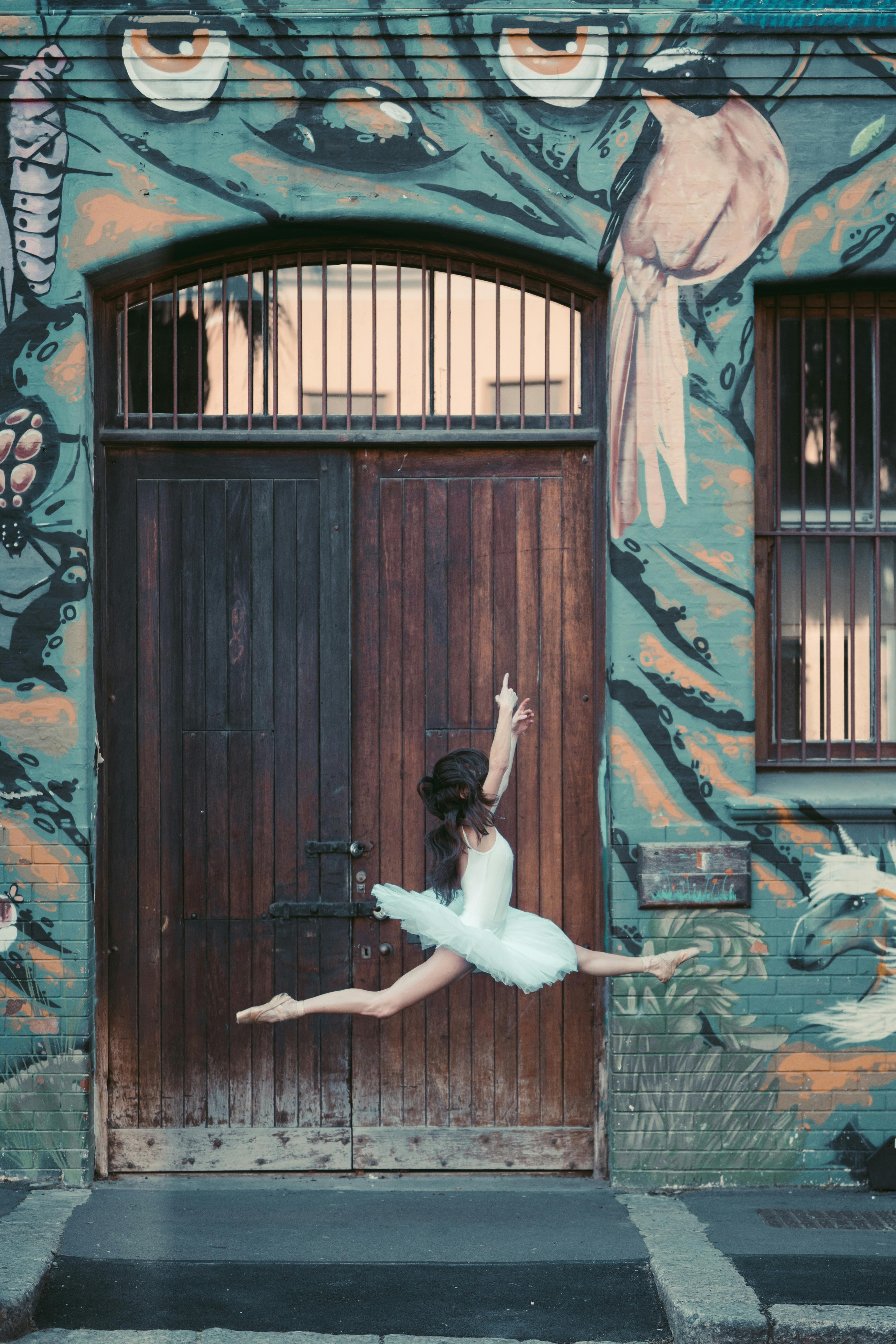 Ballet dancer elegantly leaps in front of a vibrant mural on a wooden door backdrop.