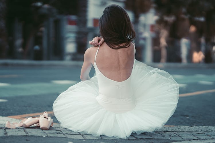 Back View Of A Ballerina Sitting On A Curb 